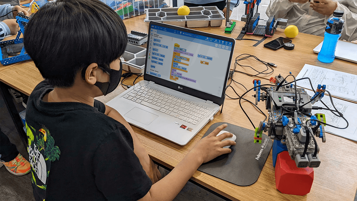 A boy works on a VEXcode IQ blocks project with a robot at his right side.