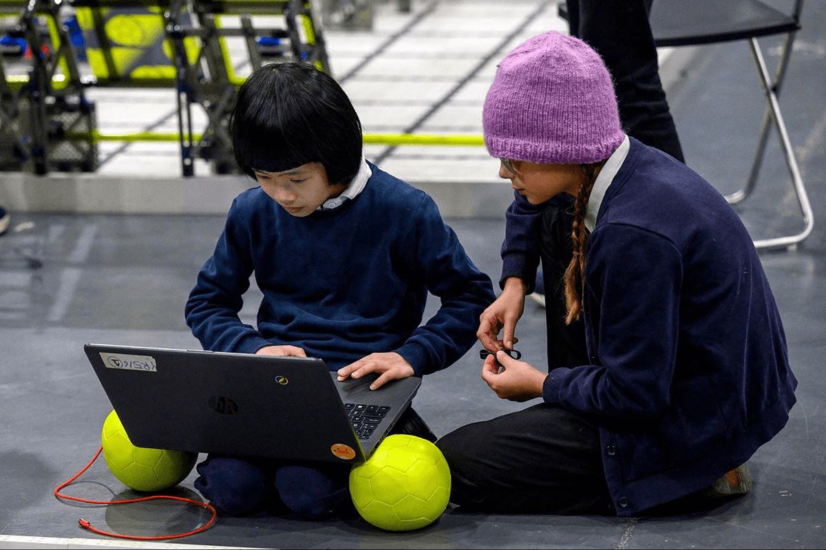 Two girls sit beside an IQ Field and look at a laptop.