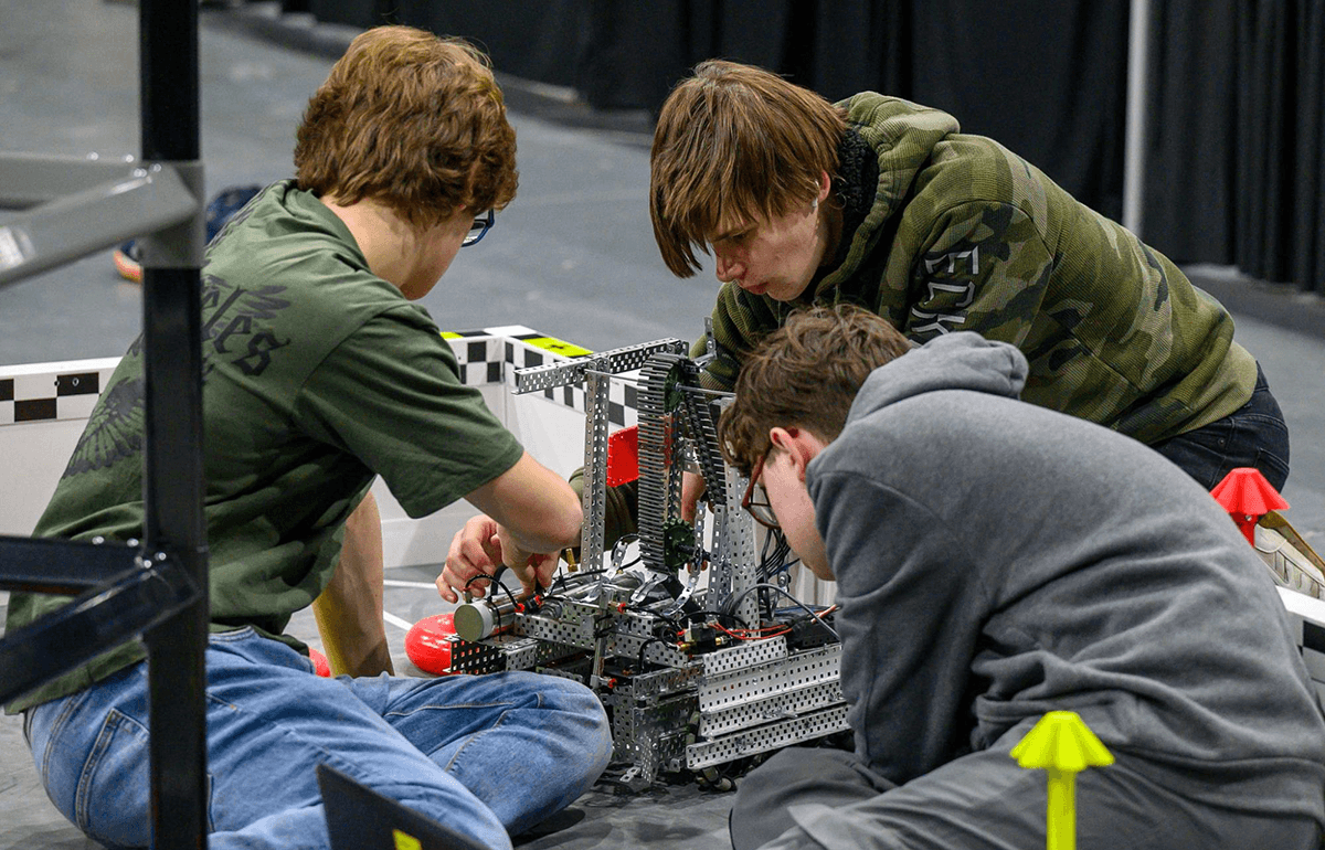 3 boys sit on a V5 Field and investigating their robot.