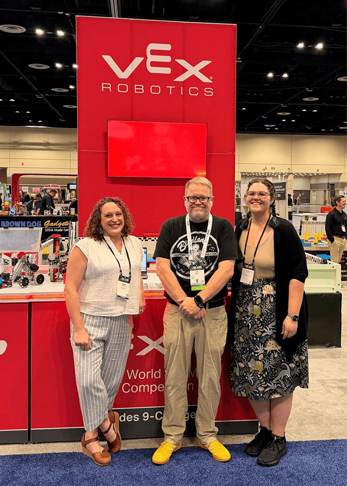 Three educators standing in front of the VEX Robotics booth at ISTELive 26.